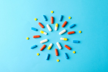 Sun made of pills on blue background, top view. Healthy vitamins.