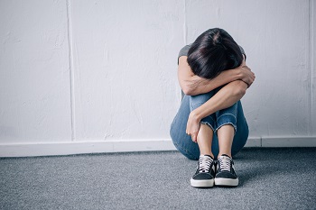 depressed lonely brunette woman sitting on floor at home with head on arms.