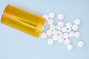 Open vial with pills scattered all over a blue background.