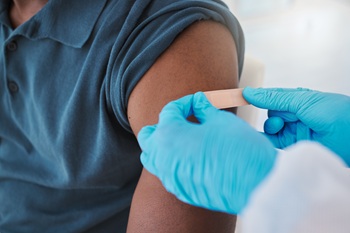 Healthcare worker putting bandaid on patient's upper arm after giving injection.